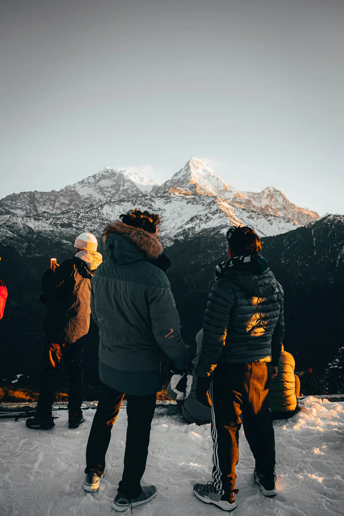 Travelers in parkas silhouetted while watching last light catch a jagged mountain summit