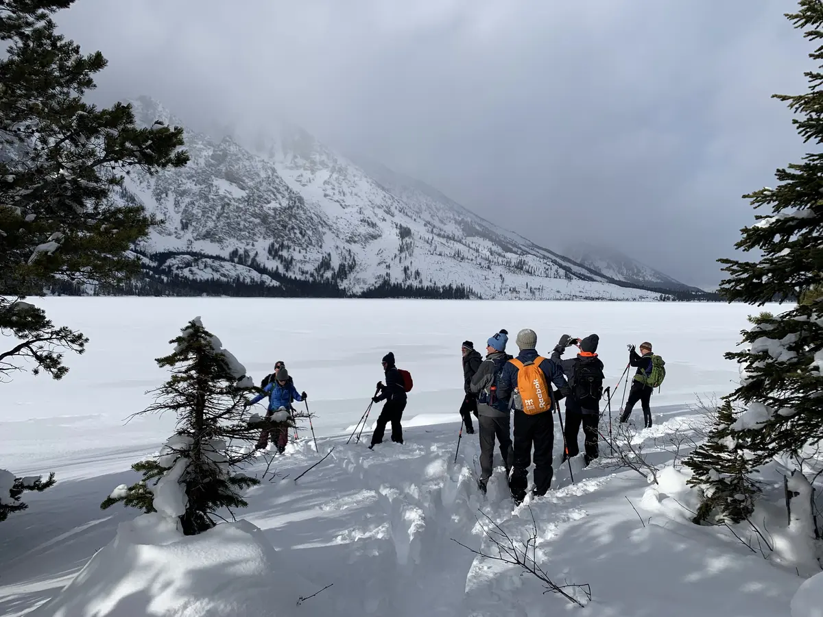 A snowshoe group gathering at the wooded edge of a frozen mountain lake