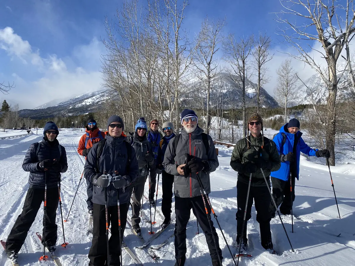 A group of cross-country skiers smiling on a snowy trail below the Teton mountains