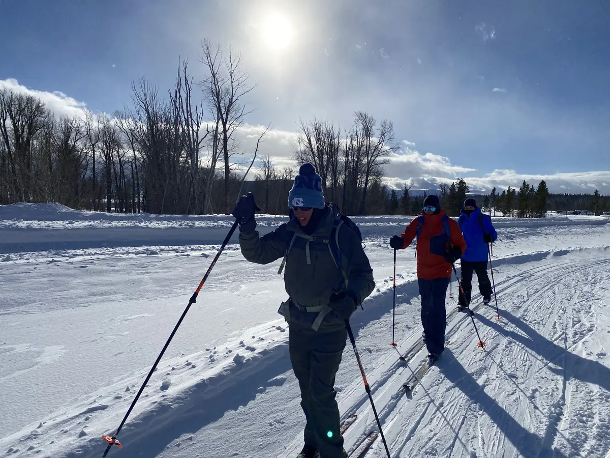 Three cross-country skiers moving along a groomed trail beneath bright winter sun