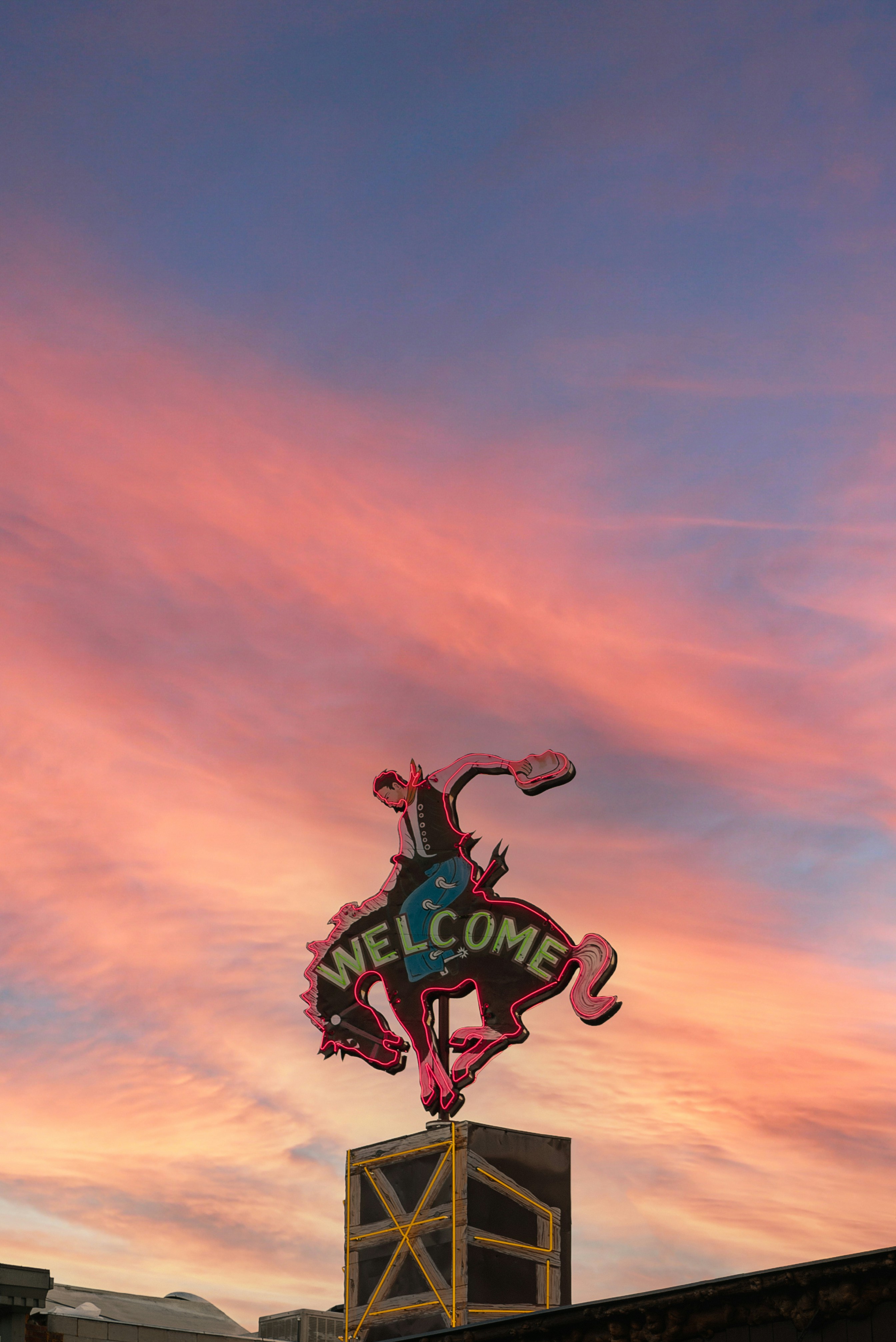Neon bucking bronco welcome sign above Jackson glowing against a pink sunset sky