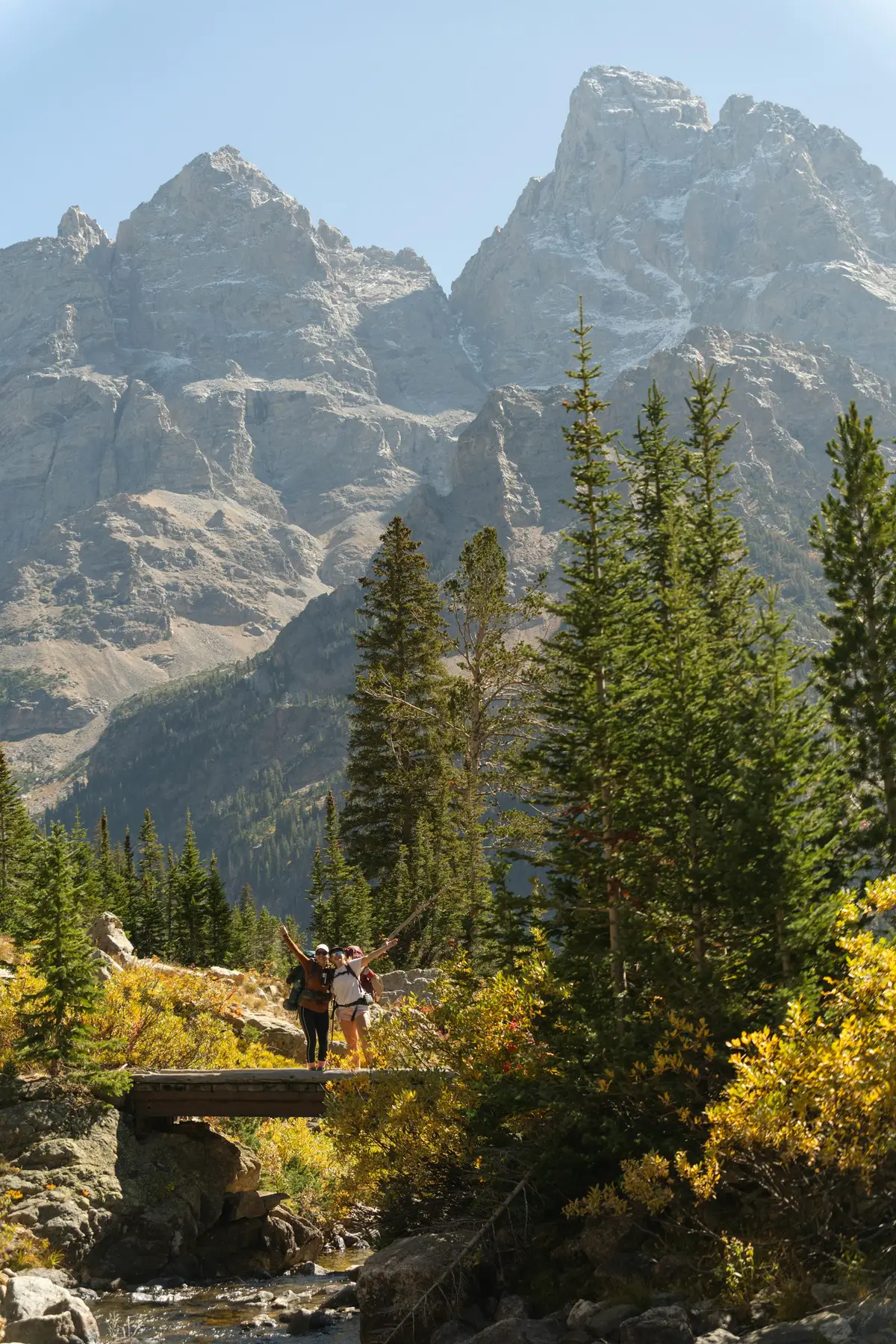 Two hikers with packs cheering on a footbridge below the Teton peaks